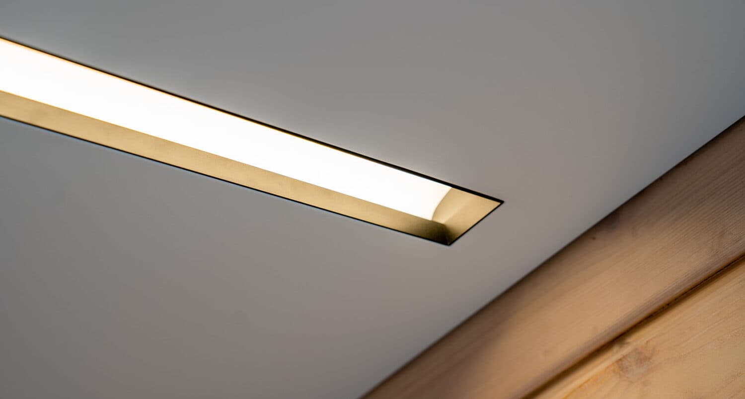 Detaliu cu profil LED încastrat în tavan extensibil, cu lumină caldă, lângă o grindă din lemn natur