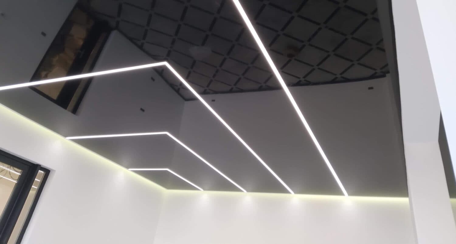 Linii LED albe paralele pe tavan extensibil alb și negru lucios cu model casetat, într-un spațiu comercial