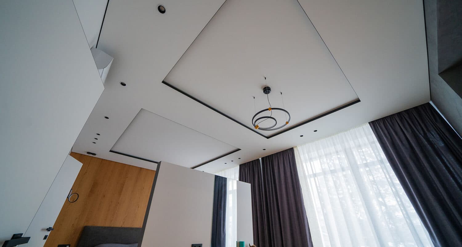 Tavan extensibil alb mat cu profile negre decorative și spoturi încastrate, într-un dormitor cu perete din lemn